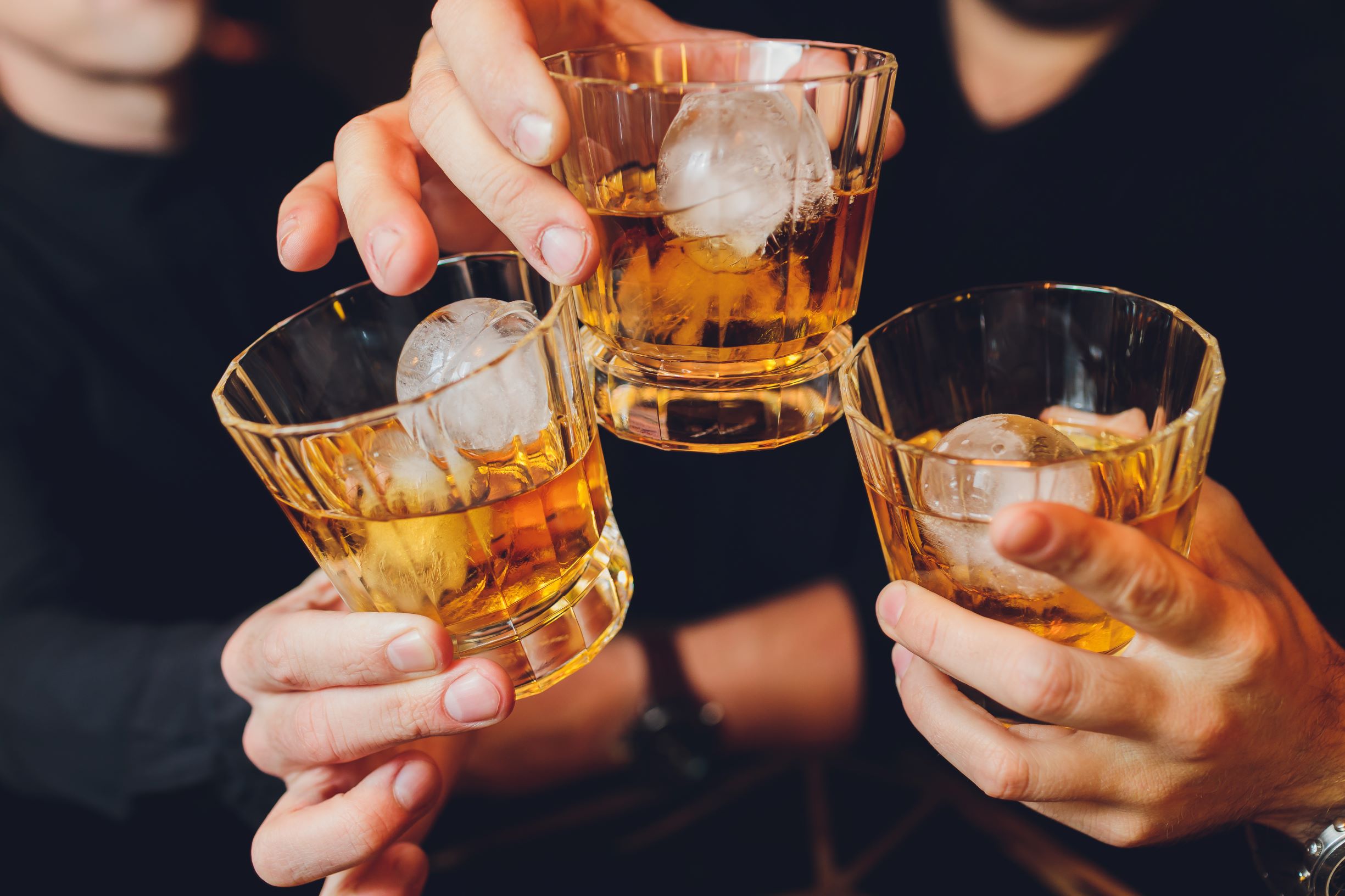 Group of friends cheers with liquor in rocks glasses with whiskey ball ice